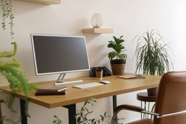 Ofis duvarının yanında bilgisayar monitörü ve ev bitkileri olan modern işyeri