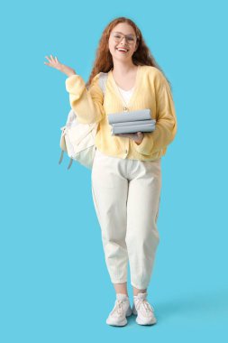 Sırt çantası ve mavi arka plan kitapları olan mutlu bir kız öğrenci.