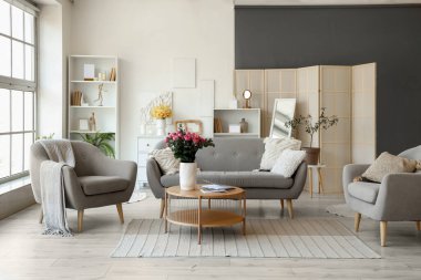 Kanepe, koltuk ve vazolarda çiçekler olan oturma odasının içinde.