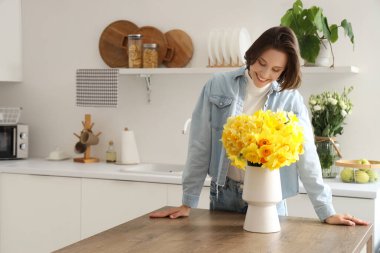 Mutfaktaki masasında nergis olan genç bir kadın.