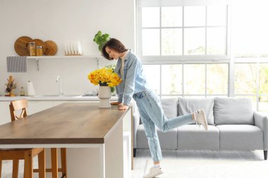 Mutfaktaki masasında nergis olan genç bir kadın.