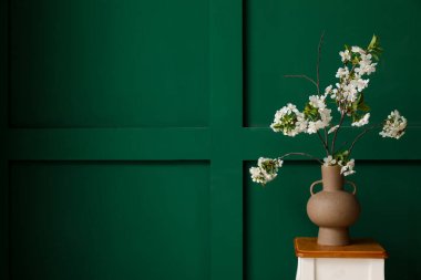 Yeşil odadaki sehpanın üzerinde çiçek açan bir vazo.