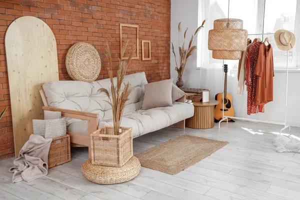 Interior of living room with comfortable sofa, pampas grass, coffee table and rack with clothes