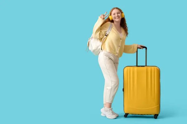 stock image Happy female student with backpack, headphones and suitcase showing victory gesture on blue background