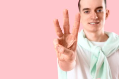 Pembe arka planda üç parmağını gösteren genç adam, yakın plan.