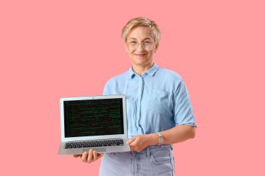 Pembe arka planda dizüstü bilgisayarı olan olgun bir kadın programcı.