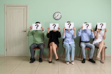 Odada iş görüşmesini beklerken ellerinde soru işaretleri olan kağıt çarşaflar tutan gençler