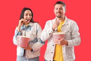 Kırmızı arka planda patlamış mısır yiyen mutlu genç çift.