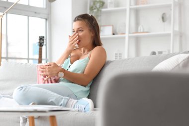 Patlamış mısırlı genç bir kadın izin gününde evde televizyon izliyor.