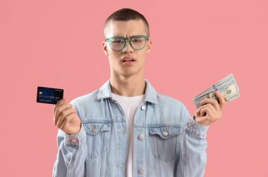 Kredi kartıyla kafası karışmış genç bir adam ve pembe arka planda dolar banknotları.