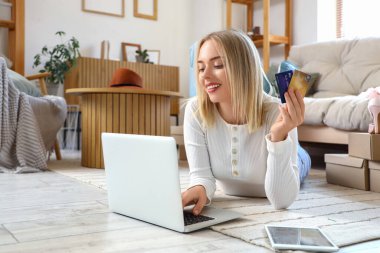 Bilgisayarı, tablet kutuları ve kredi kartları olan genç bir kadın evde online alışveriş yapıyor.