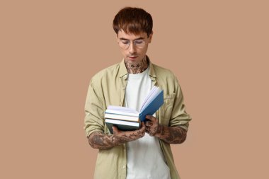 Kahverengi arka planda kitap okuyan dövmeli genç bir adam.