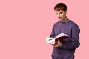 Pembe arka planda kitap okuyan dövmeli genç bir adam.