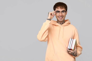 Gri arka plan kitapları olan dövmeli genç bir adam.