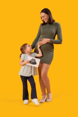 Güzel hamile anne ve sarı arka planda sonogram görüntüsü olan sevimli küçük kızı.