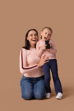 Güzel anne ve kahverengi arka planda cep telefonu olan sevimli küçük kızı.
