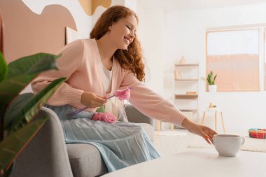 Örgü ören genç bir kadın evde çay içiyor.