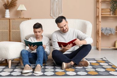 Baba ve küçük oğlu evde yerde kitap okuyorlar.