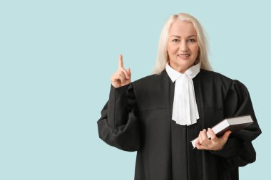 Mavi arka plandaki bir şeyi işaret eden bir kitabı olan olgun bir kadın yargıç.