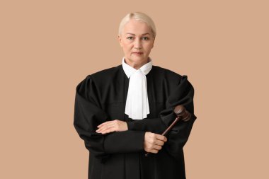 Çapraz kolları ve kahverengi arka planda tokmağı olan olgun kadın yargıç.