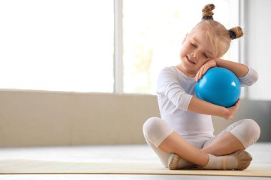 Jimnastik yapan tatlı küçük kız, spor salonunda minderde top oynuyor.