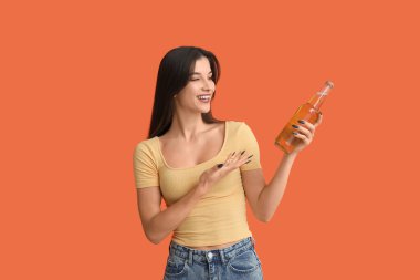 Turuncu arka planda soğuk bira şişesi olan güzel genç bir kadın.