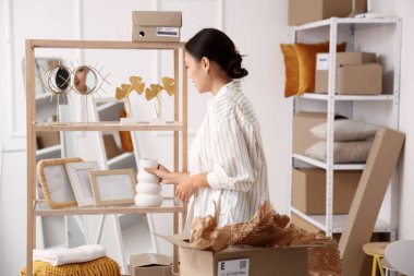 Kadın Asyalı satıcı depodaki raftan vazo alıyor.