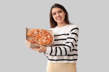 Elinde gri arka planda lezzetli pizzalar olan karton kutu tutan genç bir kadın.