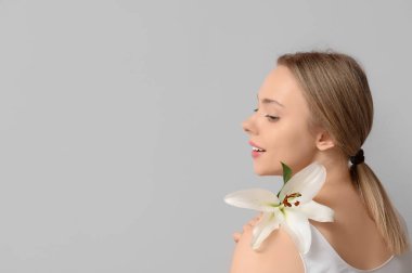 Gri arka planda zambak çiçeği olan güzel genç bir kadın.