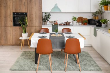 Modern mutfağın içinde yeşil bitkiler, yemek masası ve tezgahlar var.