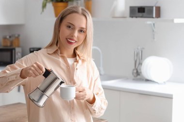 Modern mutfakta gayzer kahve makinesinden fincana espresso döken güzel bir kadın.