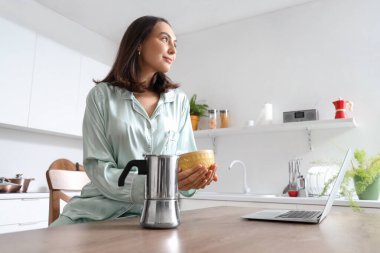 Modern mutfakta gayzer kahve makinesi, bir fincan espresso ve dizüstü bilgisayarı olan güzel bir kadın.
