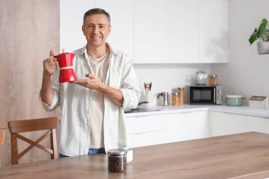 Mutfakta gayzer kahve makinesi olan olgun bir adam.