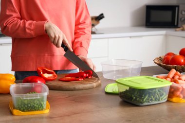 Ahşap masada donmak için kırmızı dolma biber kesen kadın.