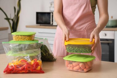 Ahşap masada dondurmak için plastik kapları sebzelerle dolduran kadın.