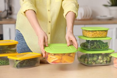 Mutfakta dondurmak için elinde sebzelerle plastik kaplar tutan bir kadın.