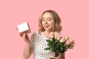 Güzel güller buketi ve pembe arka planda hediye kutusu olan genç bir kadın.