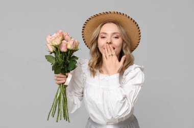 Gri arka planda güzel güllerle dolu buketi olan genç bir kadın.