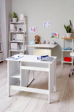 Çocuk doktorunun masaları ve çocuk çizimleriyle dolu odasının içi.