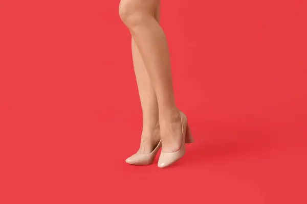 Legs of young woman in stylish beige high heels on red background