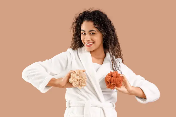 stock image Young African-American woman in bathrobe with loofahs on brown background