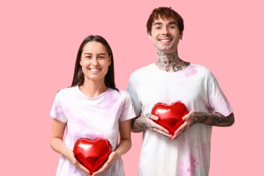 Pembe arka planda kalp şeklinde balonları olan genç bir çift.