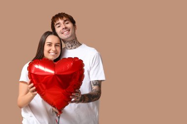 Bej arka planda kalp şeklinde hava balonu olan genç bir çift.