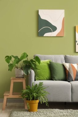 Yeşil duvarın yanındaki yastıklı, resimli ve çiçekli şık gri kanepe.