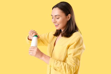 Mutlu genç bayan sarı arka planda lezzetli yoğurt şişesini açıyor.