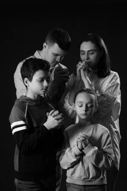 Aile karanlık arka planda birlikte dua ediyor.