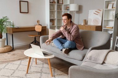 Genç adam oturma odasında dizüstü bilgisayar kullanıyor.