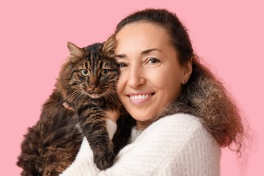 Pembe arka planda sevimli kedisi olan olgun bir kadın.