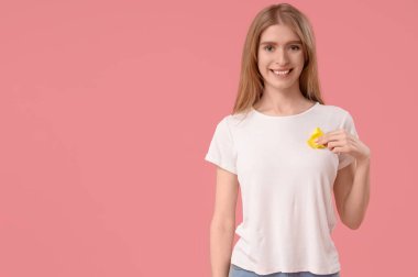 Pembe arka planda sarı farkındalık kurdelesi olan genç bir kadın. Dünya Kanser Günü
