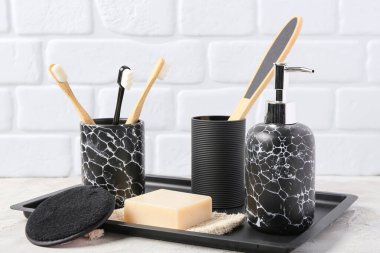 Hafif tuğla duvarın yanındaki masada banyo malzemeleri olan tepsi.